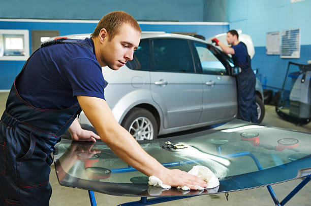 Automobile glazier adding glue on windscreen or windshield of a car in auto service station garage before installation